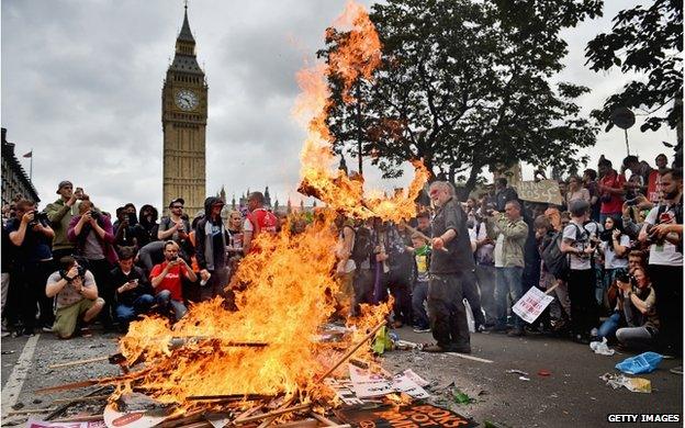 Placards being burned by anti-austerity protesters. Big Ben is visible in the background