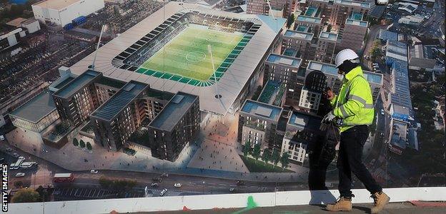 A construction worker passes an artist's impression of AFC Wimbledon's new stadium at Plough Lane