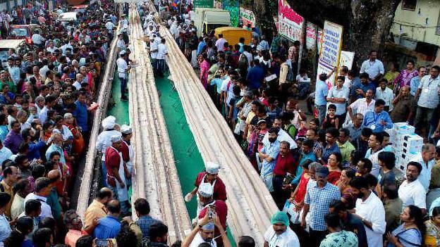 Longest cake can be seen in the street surrounded by lots of people.