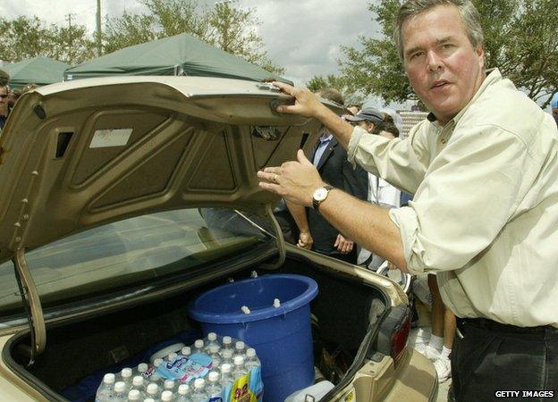 Florida Governor Jeb Bush places a case of water in the trunk of a hurricane victim's car, with his brother US President George W. Bush(not seen) to victims of Hurricane Frances 08 September 2004.