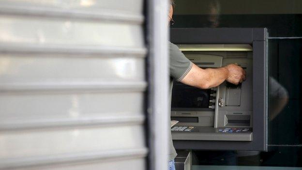 A man withdraws money at an Alpha Bank branch ATM in central Athens