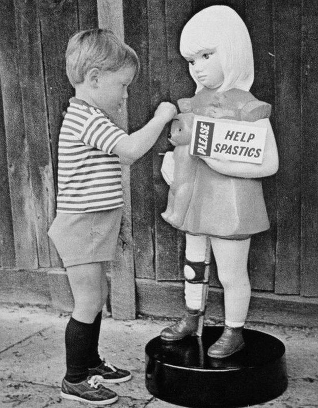 A little boy putting money in an old collection tin.