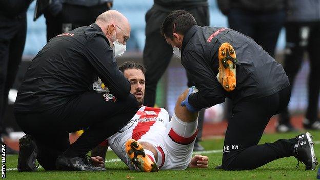 Southampton striker Danny Ings receives treatment from two physios after injuring his left knee against Aston Villa