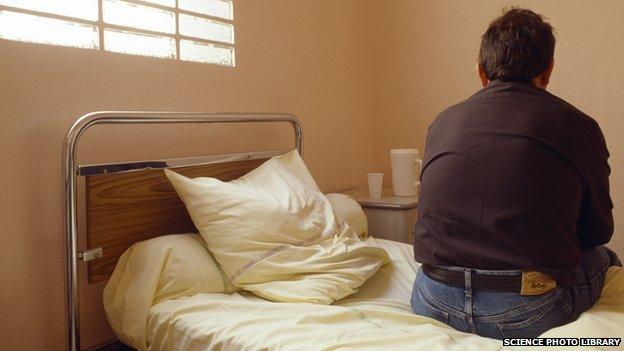 A man sits on a bed in a psychiatric ward