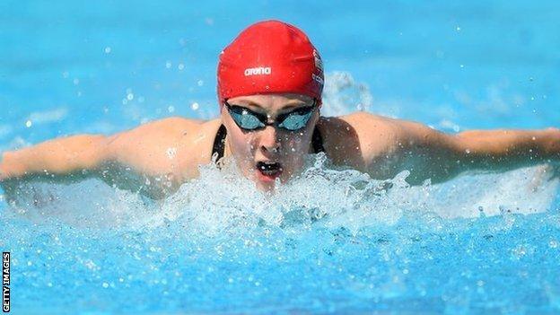 Close up photograph of Siobhan-Marie O'Connor, wearing a red swimming cap and goggles, swimming towards the camera.