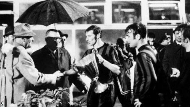 Man City skipper Tony Book being handed the trophy under an umbrella