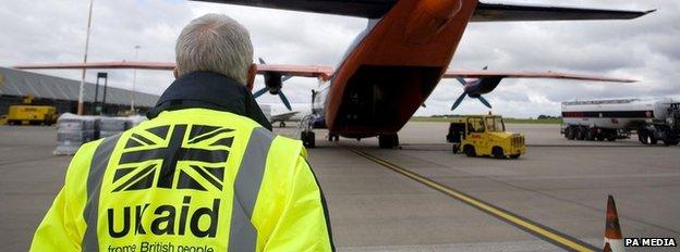 A Dfid employee wearing a UK aid hi-vis heads towards a plane