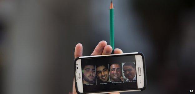 A woman in Tel Aviv holds up a pencil and a mobile phone with a picture of the four Jewish victims