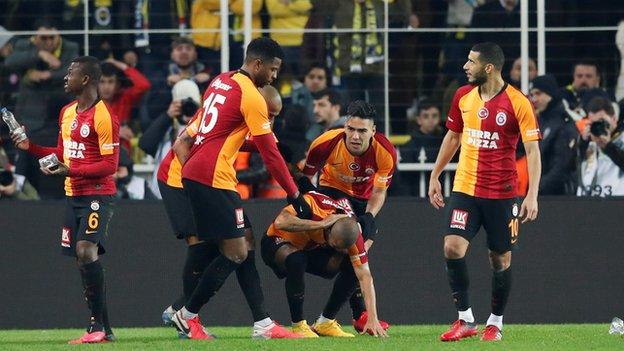 Galatasaray players take shelter from objects being thrown onto the Fenerbahce pitch