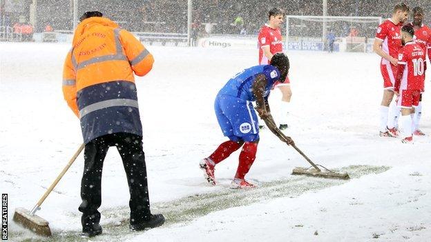 Peterborough United players help clear the lines in snow against Walsall