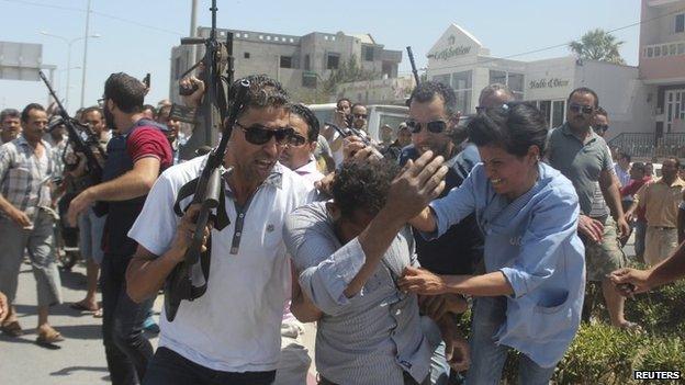 Police officers control the crowd while surrounding a man suspected to be involved in opening fire on a beachside hotel in Sousse