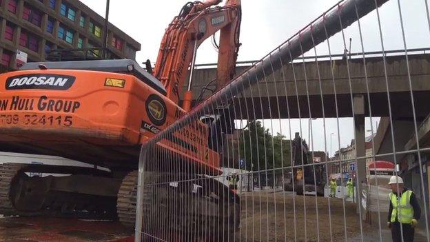 Machine prepares to knock down a bridge in the background