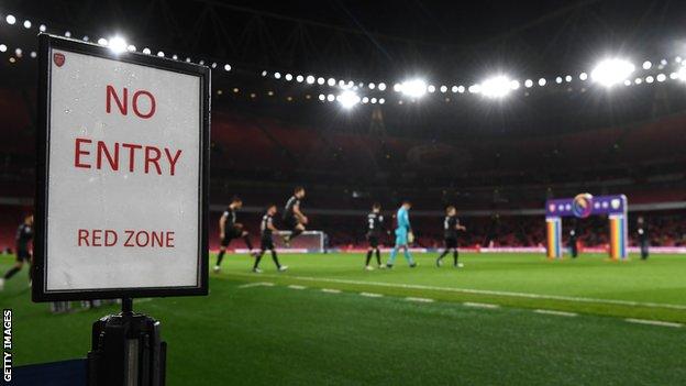 Players walk onto the pitch at Emirates Stadium with a red zone sign on display