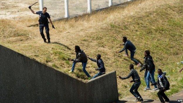 A French policemen trying to keep a group of migrants off a road near Calais