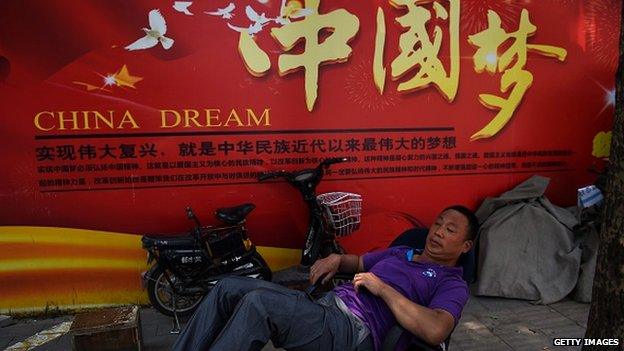 A man rests in front of a banner about the 'China Dream', Chinese President Xi Jinping's vision for China's future. The Chinese characters translate as 'To realise the revitalisation is the biggest dream in modern times of Chinese nationals'