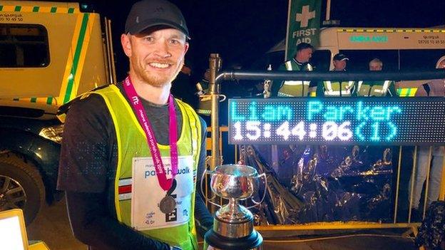 2019 Parish Walk winner Liam Parker holding the trophy with his finishing time on a screen behind