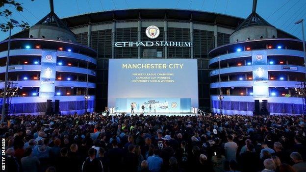 Manchester City fans gather around the stage outside Etihad Stadium awaiting the arrival of the players