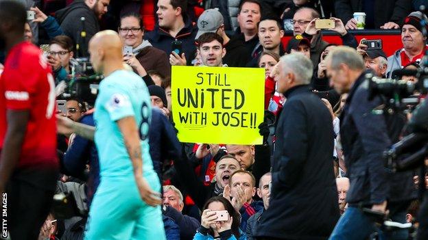 Jose Mourinho walks past a Manchester United fan sign reading "Still United with Jose"