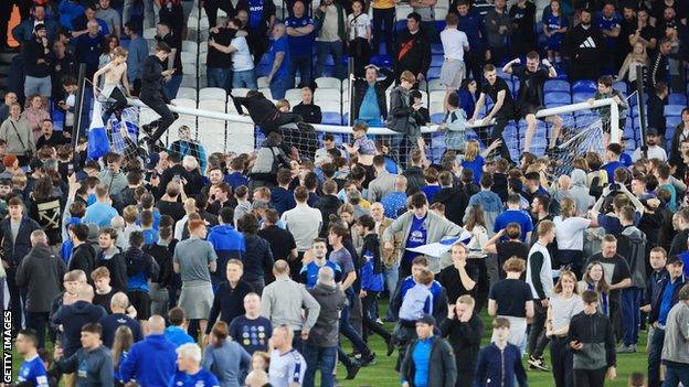 Everton fans on the pitch and on top of the goal