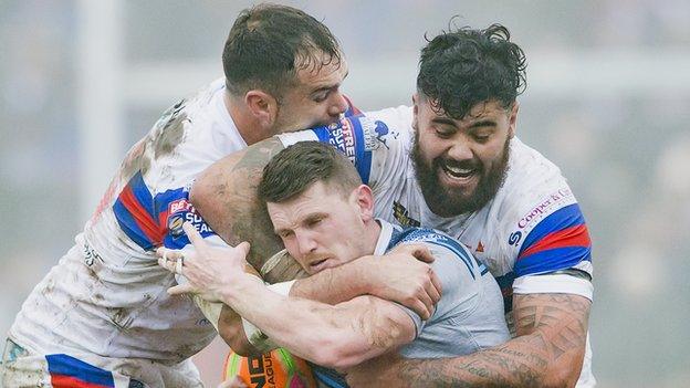 Huddersfield's Lee Gaskell is tackled by Wakefield's Anthony England & David Fifita