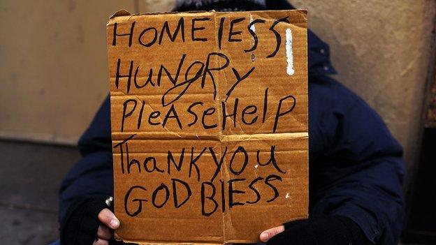 A homeless person holds up a sign