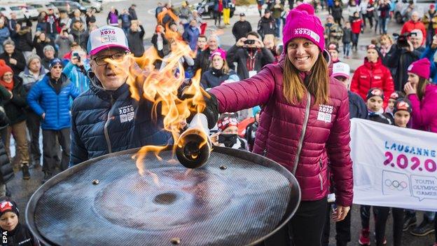 Lausanne 2020 president Virginie Faivre, right, lights the Olympic flame ahead of the Winter Youth Olympics