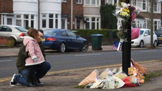 A man and young girl leaving tributes at the scene