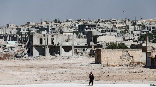 A Syrian man walks in front of destroyed buildings south Kobane, Syria