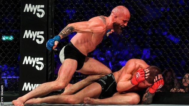 Peter Queally punches Ryan Scope on the floor of the cage