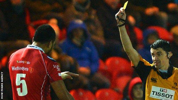 Referee Pascal Gauzere shows Maselino Paulino of Scarlets a yellow card against Northampton