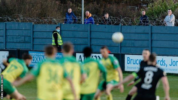 Caernarfon fans watching their team face Connah's Quay from behind the wall at the club's Oval ground