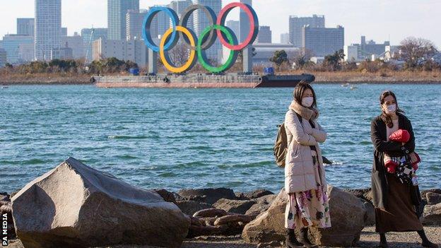 Residents with masks in front of the Olympic signs