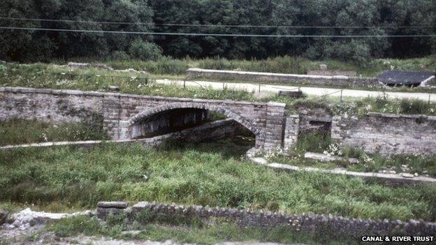 Derelict view of the Bugsworth Basin on the Peak Forest Canal, with a road bridge over a filled in and overgrown canal. Taken in 1980.