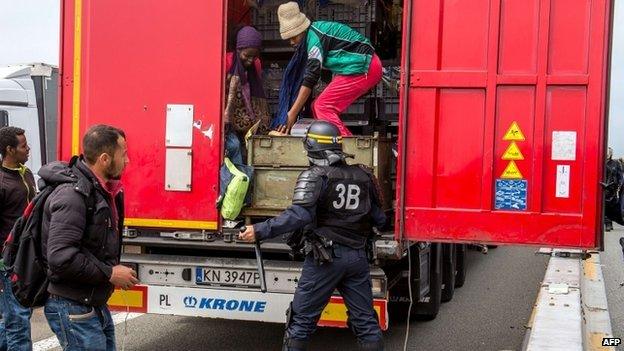 A French policeman stands behind a lorry as migrants climb off the back