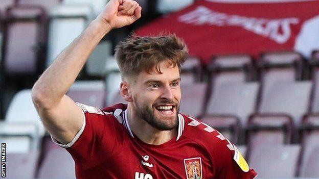 Jon Guthrie with dark hair and beard wearing a red football shirt on a football pitch