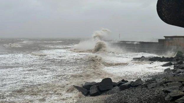 Giant waves crash against a sea wall.