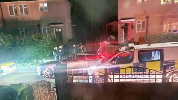 A police van is parked outside a residential area. There are people on the sidewalk standing together.