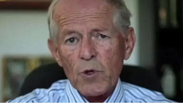 John Smyth looks on during a court hearing. He's sat on a chair and wearing a stripy shirt.