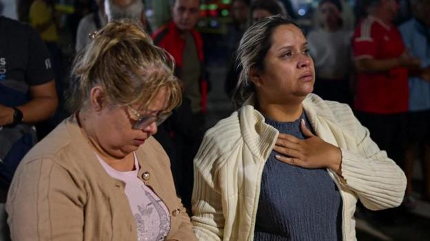 The mother and grandmother of a 18-year-old girl who is feared trapped in a collapsed building in Caracas wait as emergency workers look for her. The younger woman is holding her hand to her chest while clutching the hand of her mother.
