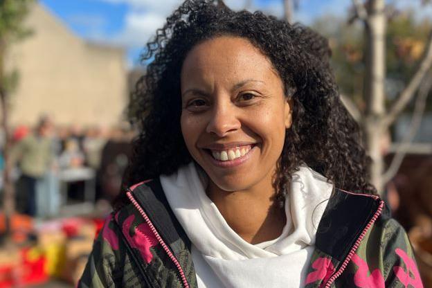 Lady with curly brown hair, a white hoody and a patterned pink, green and white jacket. She is smiling at the camera.