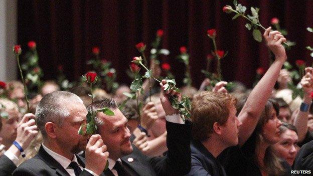 People holding up roses at the memorial gathering.