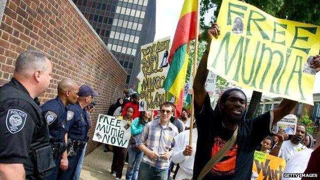 Protesters hold signs in support of Mumia Abu Jamal while police officers look on