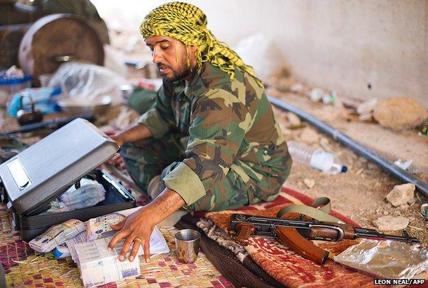 A senior figure in the NTC army with a reinforced briefcase filled with wrapped bundles of tens of thousands of Dinar