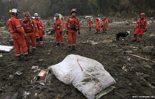 Snow falls as members of a British search and rescue team look down at the covered remains of an unidentified woman in Kamaishi, Japan