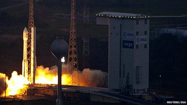 Vega rocket launching with bright smoke, next to buildings