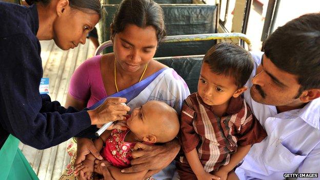 lady gives medicine to a baby with family watching