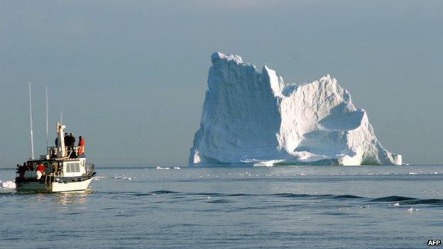A boat cruises near iceberg off the coast of Greenland