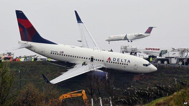 A Delta Airlines Boeing 737 lies next to a runway, tilted to one side.