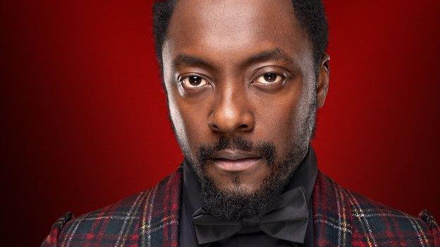 Will.I.Am in a publicity photograph for BBC's The Voice. He is wearing a smart black bowtie and a quirky, tartan dinner jacket.