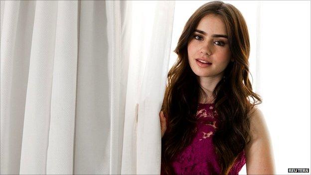 Actress Lily Collins poses with tousled brown curles amongst white curtains.